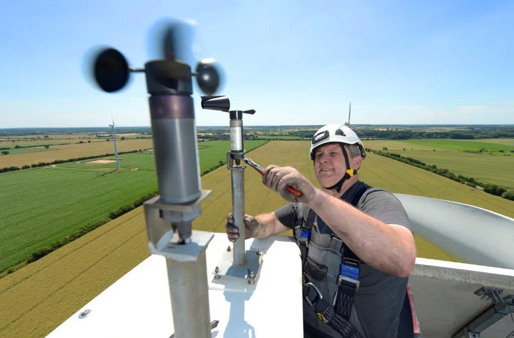 Techniker justiert ein Windmessgerät auf der Gondel einer Windkraftanlage